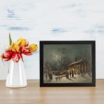 Vintage wall art of a snowy winter night with a horse-drawn sleigh, glowing lights, and people walking in front of a lit church. displayed on the wall