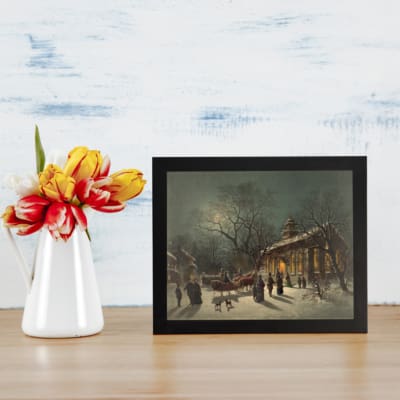 Vintage wall art of a snowy winter night with a horse-drawn sleigh, glowing lights, and people walking in front of a lit church. displayed on the wall