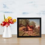 Two horses in a countryside setting with trees, grass, and soft sky tones, framed in black – vintage wall art by Infidu. displayed on the wall