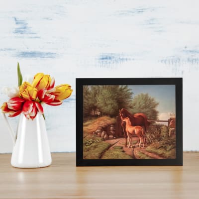 Two horses in a countryside setting with trees, grass, and soft sky tones, framed in black – vintage wall art by Infidu. displayed on the wall