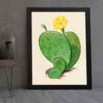 Vintage cactus wall art with a green cactus and yellow flower on a beige background, framed in black. displayed on the wall