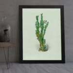 Vintage wall art of a green plant with small leaves, set against a soft light cream background, framed in black. displayed on the wall