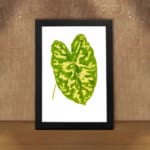 Vintage wall art of a large green tropical leaf with bright yellow streaks on a white background and black frame. displayed on the wall