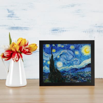 Vincent van Gogh’s The Starry Night vintage wall art shows swirling blue sky, bright yellow stars, a crescent moon, a tree silhouette, and a village. displayed on the wall