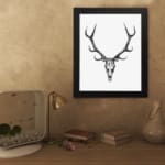 Rustic deer skull vintage wall art with black-and-white design on a grainy background. displayed on the wall in a black frame