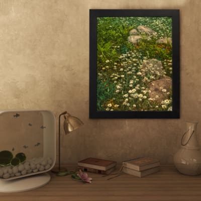 Vintage wall art of white wildflowers in a green field with stones, framed in black. displayed on the wall