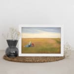 Vintage wall art of two women sitting in an open field under a bright, cloudy sky with soft green and yellow tones. displayed on the wall