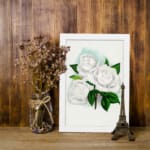Vintage white rose wall art with green leaves and soft blue background. displayed on the wall