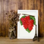 Vintage wall art of red grapes on a vine with green leaves and a white background, framed in white. displayed on the wall