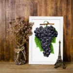 Vintage wall art print of dark purple grapes with green leaves on a white background. displayed on the wall