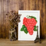 Vintage wall art of red grapes with green leaves on a white background. displayed on the wall