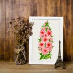 Vintage botanical wall art of pink flowers with red centers and green leaves on a soft off-white background. displayed on the wall