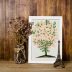 Infidu vintage wall art of a delicate pink blossom tree with green leaves and a white background. displayed on the wall