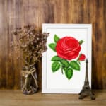 Vintage wall art of a bold red rose with green leaves on a white background, displayed on the wall