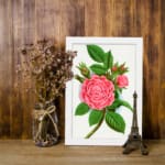 Infidu vintage wall art with blooming pink rose and green leaves in a classic white frame. displayed on the wall