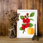 Infidu vintage wall art featuring vibrant red flowers and lush green leaves against a white background with a sleek black border. displayed on the wall art in a white frame