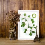 Infidu vintage wall art featuring delicate white flowers and vibrant green leaves against a white background displayed on the wall art in a white frame