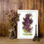 Vintage floral wall art with purple blossoms, yellow centers, and green leaves on a white background. displayed on the wall