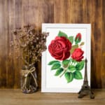 Vintage botanical wall art of red roses with green leaves on a white background by Infidu. displayed on the wall