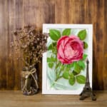 Infidu vintage wall art with a pink rose in full bloom and green leaves on a soft watercolor background. displayed on the wall