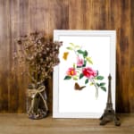 Vintage art of pink and red flowers with green leaves, two orange and brown butterflies, framed in white. displayed on the wall