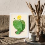 Vintage cactus wall art with a green cactus and yellow flower on a beige background, framed in white. displayed on the wall