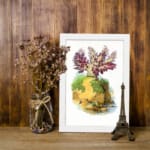 Vintage wall art of a plant with purple and red leaves on a mossy rock, set against a cream background and framed in white. displayed on the wall