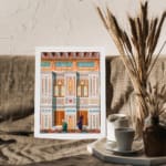 Vintage architectural wall art with two traditional figures, colorful tile patterns, and detailed building elements in white frame. displayed on the wall