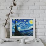 Vincent van Gogh’s The Starry Night vintage wall art shows swirling blue sky, bright yellow stars, a crescent moon, a tree silhouette, and a village. displayed on the wall