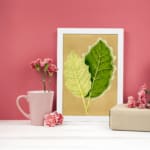 Infidu vintage wall art featuring two detailed botanical leaves in light and dark green against a soft beige background. displayed on the wall art in a white frame