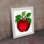 Vintage red apple wall art with green leaves on a white background, perfect for kitchen or dining room decoration. displayed on the wall