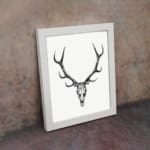 Rustic deer skull vintage wall art with black-and-white design on a grainy background. displayed on the wall in a white frame