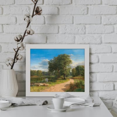 Vintage wall art of a countryside scene with a dirt path, tall trees, green grass, calm water, and a bright blue sky. Perfect for rustic decor. displayed on the wall in a white frame
