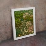 Vintage wall art of white wildflowers in a green field with stones, framed in white. displayed on the wall