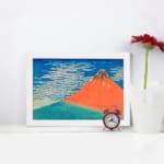 Vintage wall art of Mount Fuji by Hokusai with red mountain, blue sky, and white clouds. displayed on the wall