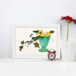 Infidu vintage wall art featuring a blue-green vase with bright yellow flowers, lush green leaves, and delicate purple berries against a light background. displayed on the wall art in a white frame