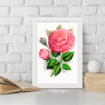 Vintage wall art with a pink rose in full bloom, a rosebud, and green leaves on a white background with a white frame. displayed on the wall
