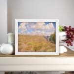 Vintage wall art of a golden grass field under a blue sky with white clouds and trees on the side displayed on the wall