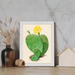 Vintage cactus wall art with a green cactus and yellow flower on a beige background, framed in white. displayed on the wall