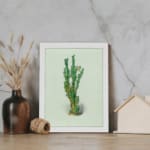 Vintage wall art of a green plant with small leaves, set against a soft light cream background, framed in white. displayed on the wall
