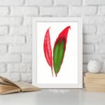 Vintage wall art of bold red and green tropical leaves in a white frame displayed on the wall