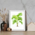 Vintage wall art featuring a green palm plant with curved leaves, framed in white, adds a fresh tropical feel to any room. displayed on the wall