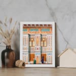 Vintage architectural wall art with two traditional figures, colorful tile patterns, and detailed building elements in white frame. displayed on the wall