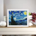 Vincent van Gogh’s The Starry Night vintage wall art shows swirling blue sky, bright yellow stars, a crescent moon, a tree silhouette, and a village. displayed on the wall