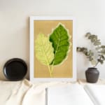 Infidu vintage wall art featuring two detailed botanical leaves in light and dark green against a soft beige background. displayed on the wall art in a white frame