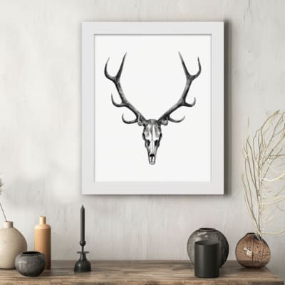 Rustic deer skull vintage wall art with a black-and-white design on a grainy background. displayed on the wall in a white frame