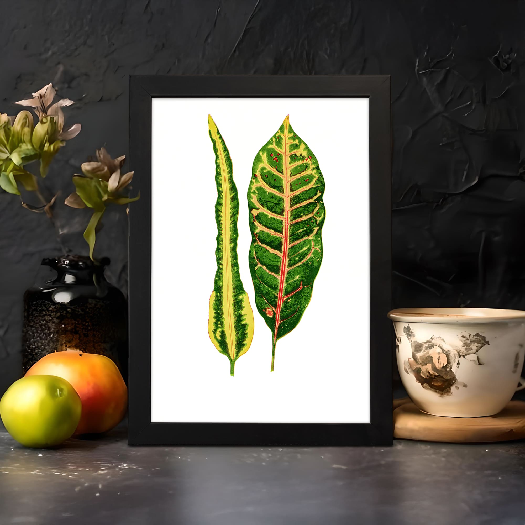 Vintage wall art of two colorful botanical leaves in green, yellow, and red with a white background and black frame. displayed on the wall