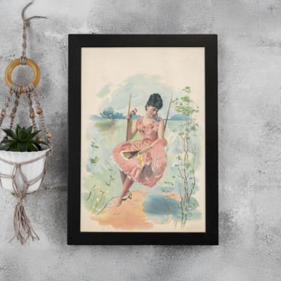 Vintage wall art of a woman in a pink dress sitting on a swing with a scenic landscape, framed in black for a classic and elegant look. displayed on the wall