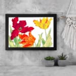 Vintage floral wall art with red, orange, and yellow tulips, green leaves, and a black frame on a white background. displayed on the wall