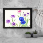 Infidu Vintage Floral Wall Art with blue, purple, and white flowers, green stems, and a black frame on a light background. displayed on the wall